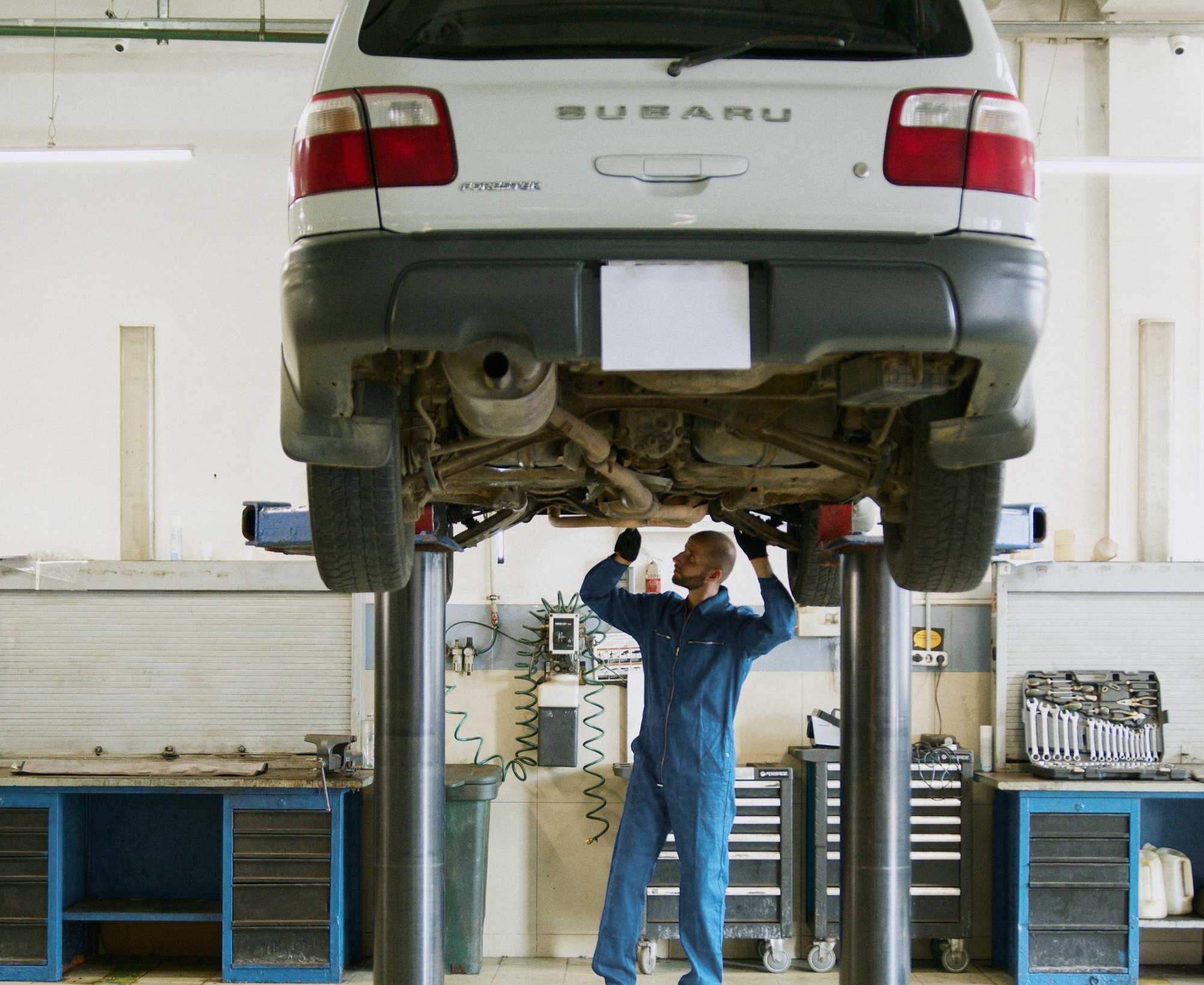 Subaru Forester на двостійковому підйомнику, майстер оглядає авто знизу